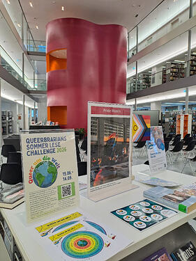 Medienpräsentationswagen in einer Bibliothek zum Pride Month mit Aufsteller zur Queerbrarians-Sommer-Lesechallenge
